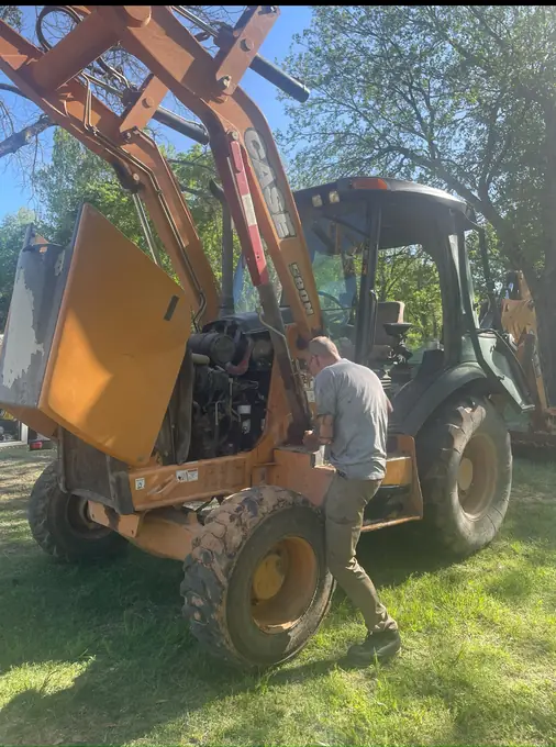 Technician working under the hood of a Case backhoe loader